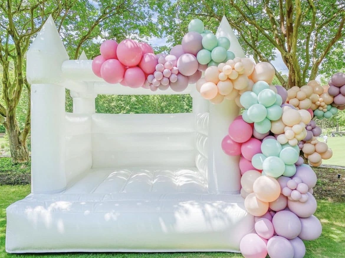 White bounce house with pastel balloon garland rental in Miami